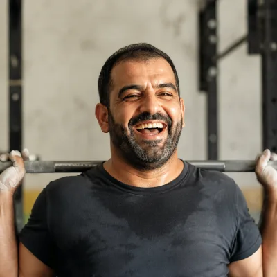 A man in his thirties racking a barbell in a gym, chalk on his hands